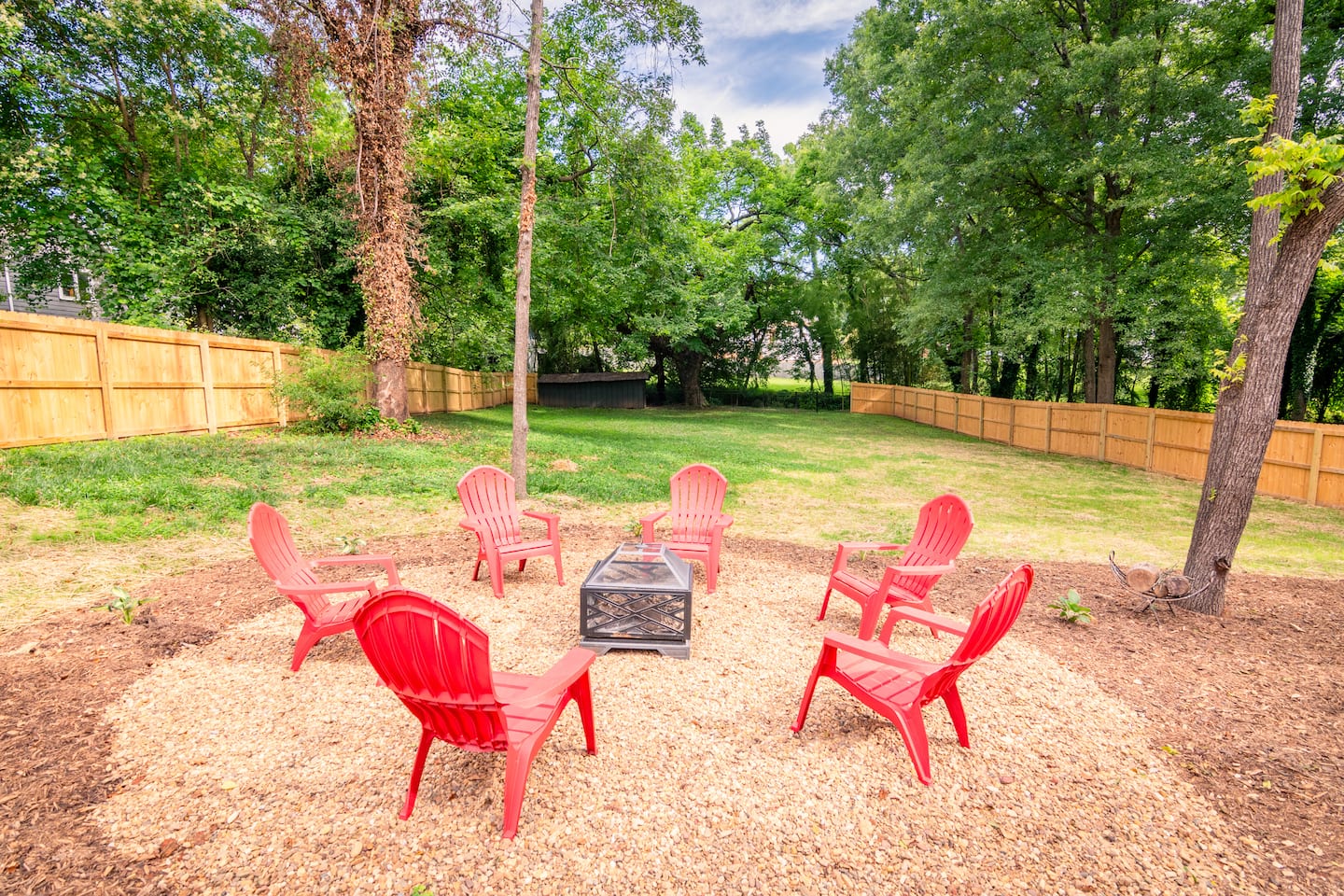 Six red chairs around a fire pit in the large fenced backyard